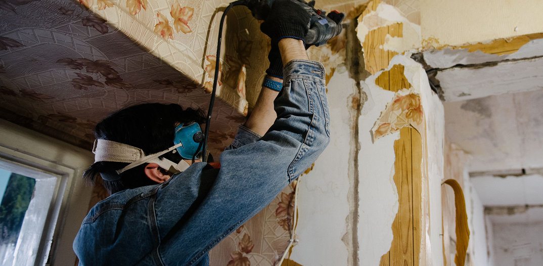 Renovation contractor wearing protective safety goggles using a rotary power tool during wall demolition and insulation removal.