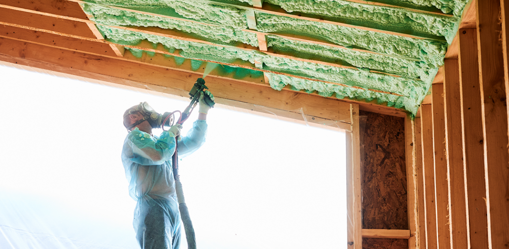 Professional insulation contractor spraying green spray foam insulation between wooden ceiling joists during a home renovation